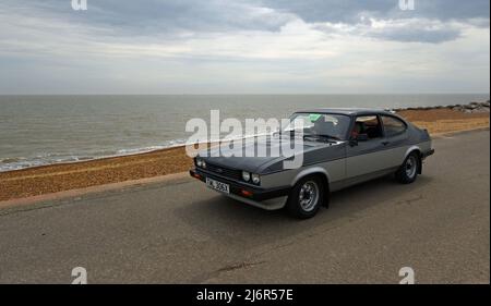 Der klassische Ford Capri in Grau und Silber wird entlang der Strandpromenade und dem Meer im Hintergrund gefahren. Stockfoto