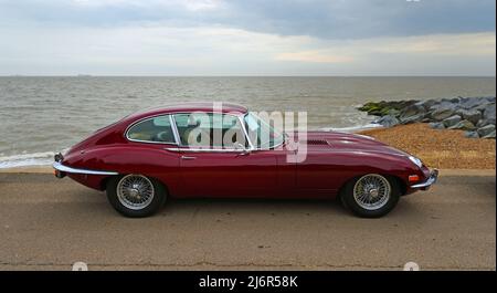 Classic Red E Typ Jaguar geparkt an Strandpromenade Strand und Meer im Hintergrund Stockfoto