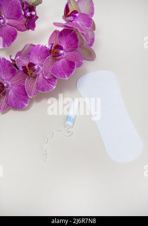 Hygieneartikel während deiner Zeit wird ein Tampon oder Pad mit einer violetten Orchideenblume platziert Stockfoto