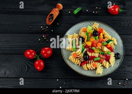 Penne-Pasta mit Gemüse, Erbsen, Paprika, Tomaten, Sauce, Mozzarella-Käse auf schwarzem Holzboden. Italienische Pasta mit Gemüse und sp Stockfoto