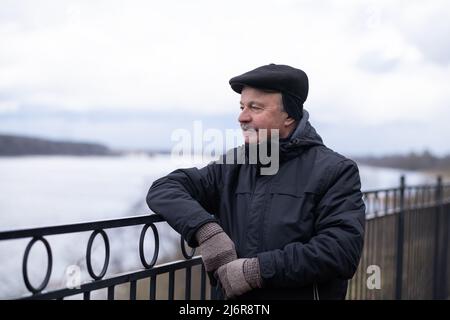 Leitender kaukasischer Mann, der bei kaltem Herbstwetter fröhlich am Flussufer steht. Stockfoto