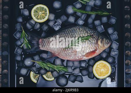 Kochen von Fisch, rohem Fisch auf einem Backblech mit Eiswürfeln, Zitronenscheiben und Rosmarinzweigen Stockfoto