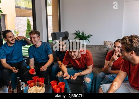 Freunde sehen sich ein Fußballspiel im Fernsehen an und kämpfen um ihr Team. Gruppe junger Menschen auf einer Party. Stockfoto