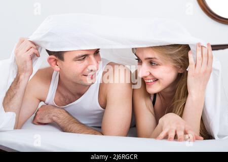 Junges Paar im Bett mit Laken bedeckt. Stockfoto