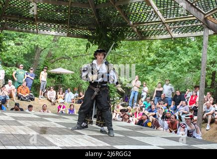 Kämpfer in mittelalterlichem Kostüm sieht erstaunt aus, als eine Kämpferin ihn mit Schwert von hinten ansteckt und die Leute Renassiane Festival Muskogee OK USA May 22 Stockfoto