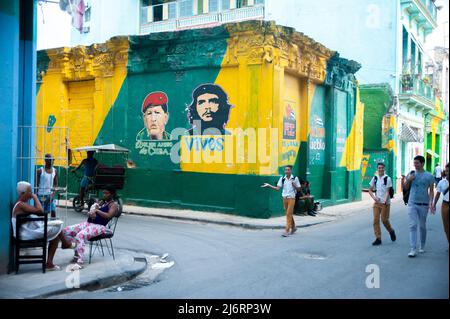 Kubanische Schuljungen gehen durch eine Straßenecke in der Nähe von Bildern von Hugo Chávez und Che im alten Havanna, Kuba, vorbei an einer jungen Mutter, die ihr neugeborenes Kind hält. Stockfoto