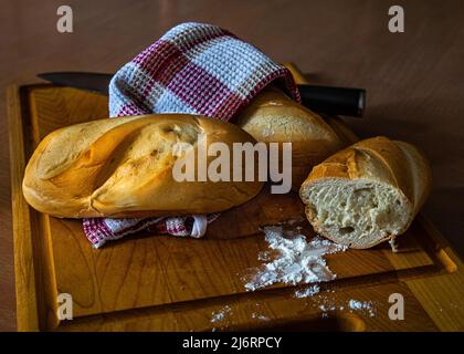 Frisches, leckeres Brot, Brötchen, ein Küchenmesser mit etwas Mehl auf einem Schneidebrett. Stockfoto