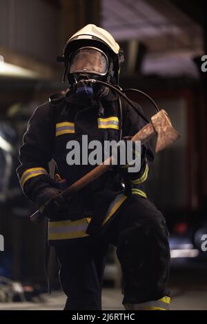 Weibliche Feuerwehrmann Porträt trägt komplette Ausrüstung, Sauerstoff-Maske, und eine Axt. Rauch und Feuer Lastwagen im Hintergrund. Stockfoto