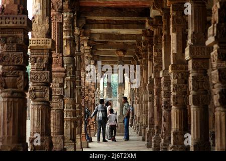 Besucher der Quwwat ul-Islam Moschee, fotografiert in einer mit geschnitzten Säulen geschmückten Gasse im Qutab Minar Komplex in Mehrauli, Süd-Delhi, Delhi, Indien. Stockfoto