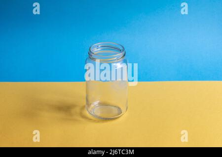 Leeres Glas ohne Deckel mit ukrainischer Flagge im Hintergrund Stockfoto