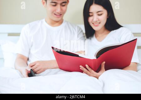 asiatische Paare planen für die Zukunft suchen Bücher, Kauf Lebensversicherung, Kauf von Häusern, Blick auf Hochzeitsfotos. Stockfoto