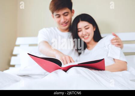 asiatische Paare planen für die Zukunft suchen Bücher, Kauf Lebensversicherung, Kauf von Häusern, Blick auf Hochzeitsfotos. Stockfoto