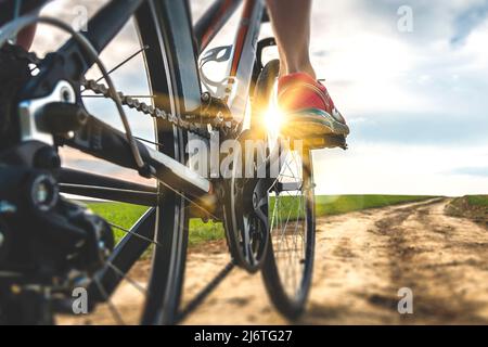 Fuß auf dem Fahrradpedal bei Sonnenuntergang. Nahaufnahme der Rückansicht des Radfahrers, der in die Pedale tritt. Fahrrad auf der Straße. Stockfoto