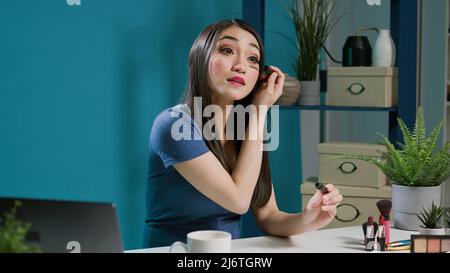 Asiatischer Content Creator testet Mascara-Produkt auf Vlogging-Kamera, Dreharbeiten Schönheit Tutorial mit Make-up-Tipps. Asiatische Frau tut Glam Kosmetik Empfehlung, Online-Social-Media-Übertragung. Stockfoto