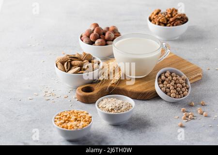Gemüsemilch in einem Becher auf dem Hintergrund von Schüsseln mit Nüssen, Haferflocken und Hülsenfrüchten. Eine Alternative zu Milchprodukten. Stockfoto
