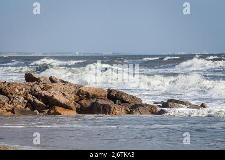 Felsen am Strand auf einer kleinen Insel im Naturschutzgebiet Ria Formosa mit dem welligen Atlantik und der Stadt Monte Gordo im Hintergrund Stockfoto