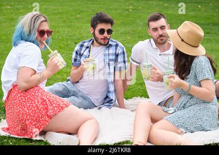 Eine Gruppe von glücklichen Freunden, die im Park reden und erfrischende Getränke trinken. Stockfoto