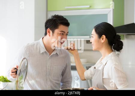 In der Familienküche hob der Ehemann den Deckel des Suppentöpfels und die Frau schaufelte einen Löffel voll für ihn zum probieren - Stockfoto Stockfoto