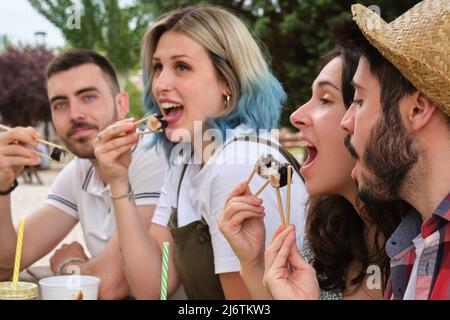 Eine Gruppe glücklicher Freunde, die lächeln und Sushi essen, die in einem Park ein Picknick machen. Stockfoto