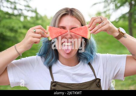 Junge glückliche Frau klebte ihre Zunge mit Wassermelonenscheiben auf ihre Augen. Stockfoto