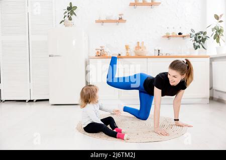 Happy Athletic Mädchen und Tochter tun Yoga in der Küche, Fitness-Instruktor, attraktive weibliche Trainer in Sportbekleidung, Meditation zu behandeln Stockfoto