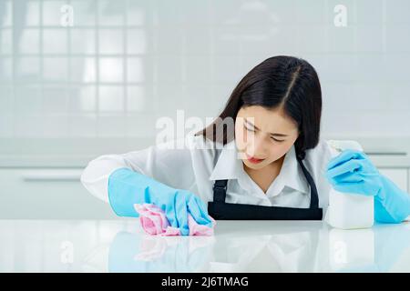 asiatische Frau trägt Gummi schützende blaue Handschuhe stehende Reinigung mit Produkten und Ausrüstung Küchenreiniger. Stockfoto