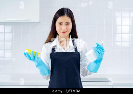 asiatische Frau trägt Gummi schützende blaue Handschuhe stehende Reinigung mit Produkten und Ausrüstung Küchenreiniger. Stockfoto