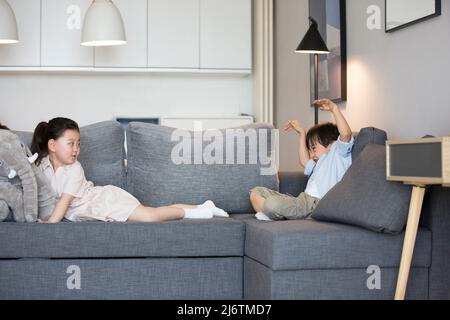 Ein kleines Mädchen und ein kleiner Junge sitzen auf der Couch im Wohnzimmer und spielen ein Spiel - Stock photo Stockfoto