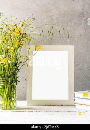 Modellerstellung. Weißer Rahmen auf weißem Holztisch mit grauem Betonhintergrund und wilden Frühlingsblumen Stockfoto