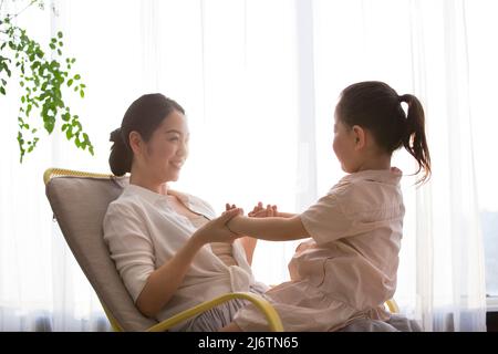 Ein kleines Mädchen sitzt auf dem Schoß ihrer jungen Mutter, während sie den Schaukelstuhl schaukeln, Kinderlieder singen und Märchen erzählen - Stockfoto Stockfoto