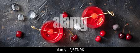 Cocktail garniert mit Kirschpanorama, frischem Preiselbeersaft mit Eis auf dunklem Grund, zwei Gläsern Stockfoto