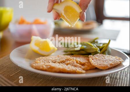 Zitrone auf veganes Kichererbsenschnitzel drücken Stockfoto