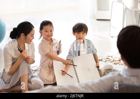 Ein Junge und ein Mädchen erzählen ihrem Vater von den Zeichnungen ihrer Kinder, während ihre Mutter begeistert auf ihr Stockfoto schaut Stockfoto