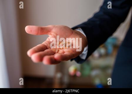 Goldene Eheringe auf der Handfläche des Bräutigams am Hochzeitstag. Stockfoto