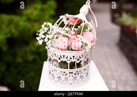 Weißer Käfig mit natürlichen Rosen als Dekoration auf Hochzeit. Stockfoto