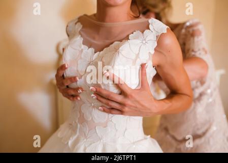 Wunderschöne, blonden Braut in Weiß Luxus Kleid ist bereit für die Hochzeit. Morgen Vorbereitungen. Frau setzen auf Kleid Stockfoto