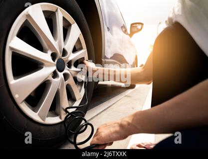 Frau bläst den Reifen auf. Frau, die den Reifendruck überprüft und Luft in den Reifen des Autorads pumpt. Autowartung zur Sicherheit vor der Reise. Stockfoto