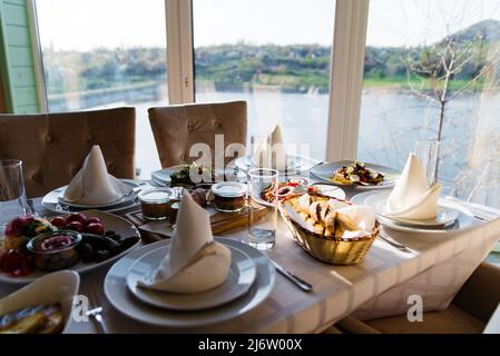 Schöner festlicher Tisch, der für das Hochzeitsessen zu Hause oder im Restaurant serviert wird. Jede Menge verschiedene Speisen und Besteck. Langer Tisch bedeckt Stockfoto