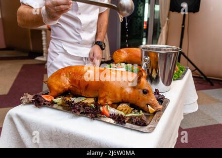Speisekarte im Restaurant. Gebackenes Spanferkel ganz auf einem Stein dekorativen Brett mit Obst und Physalis. Draufsicht. Stockfoto