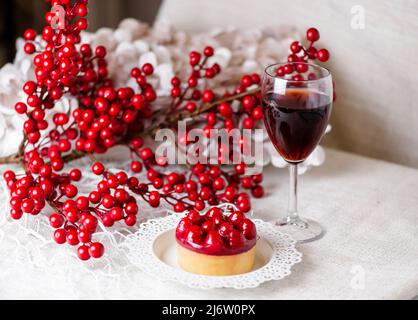 Ein Glas Rotwein, Süßigkeiten und ein Zweig mit roten Beeren Stockfoto