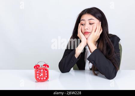 Asiatische Geschäftsfrau sitzt am Schreibtisch im Büro mit Wecker. Stockfoto