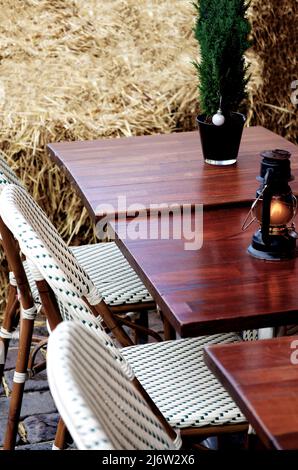 Street Cafe mit Korbstühlen, Holztischen, Weihnachtsdekoration und Strohbriketts als Nahaufnahme des Zauns Stockfoto