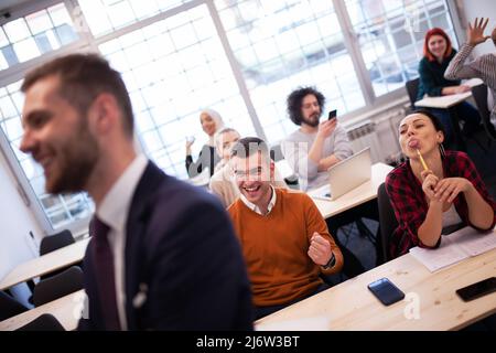 Multiethnische Studenten, die sich über den Dozenten in einem Klassenzimmer hinter seinem Rücken lustig machen. Intelligente junge Menschen studieren an einer Hochschule. Stockfoto
