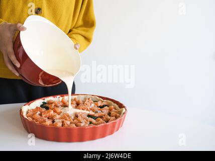 Die Frau gießt Quiche mit einer Mischung aus Eiern und Rahm. Quiche mit Lachs. Kochen. Stockfoto