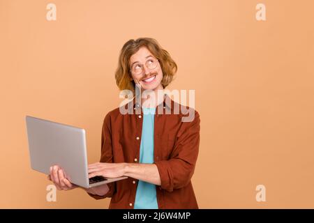 Porträt eines gutaussehenden fröhlichen nachdenklichen trendigen rothaarigen Kerl mit Laptop denken Kopieplatz isoliert über beige Pastellfarben Hintergrund Stockfoto