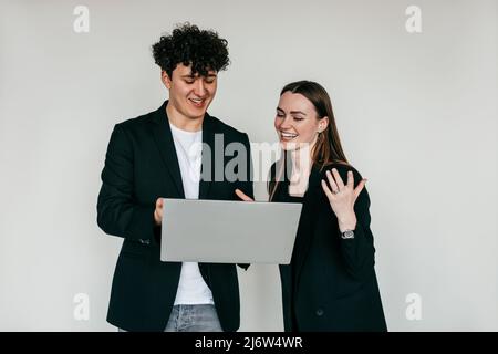 Porträt eines jungen überemotionalen Paares in schwarzer Kleidung. Junger fröhlicher Mann mit Laptop in der Nähe einer fröhlichen Frau, die sich die Hände schüttelt. Stockfoto