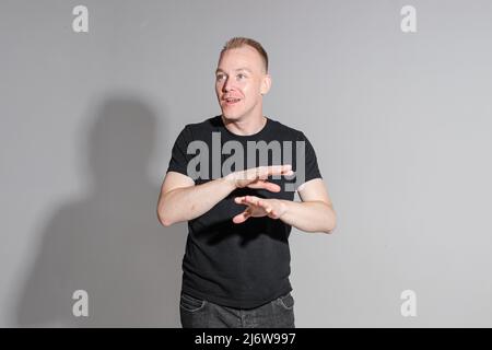 Lebhafter kaukasischer Mann in schwarzem Hemd posiert auf grauem Hintergrund Stockfoto