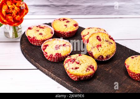 Auf einem alten Holzbrett mit Blumenstrauß wurden mehrere Johannisbeeren-Muffins serviert Stockfoto