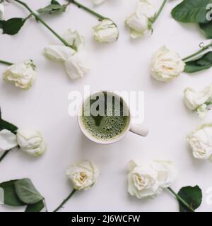 Schöne Komposition mit einer Tasse Matcha-Tee und Blumen auf weißem Hintergrund. Flatlay, Draufsicht, Kopierbereich. Stockfoto