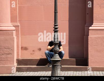 04. Mai 2022, Rheinland-Pfalz, Mainz: Hinter einer Laterne versteckt, macht ein Mann eine Mittagspause bei Sonnenschein auf den Stufen der barocken Hallenkirche St. Peter. Foto: Frank Rumpenhorst/dpa Stockfoto